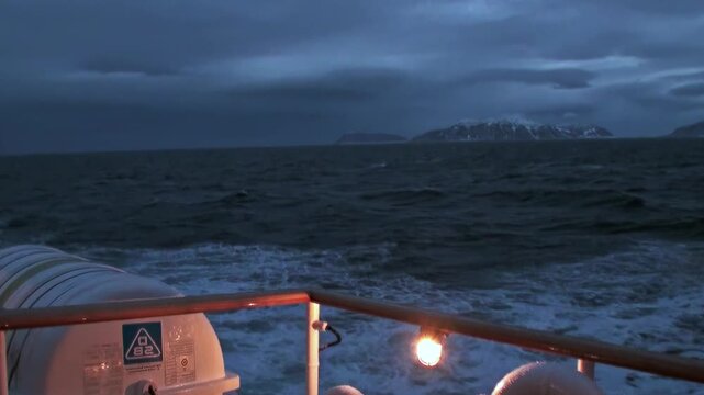 A ship crosses the Arctic Ocean beside snow-covered mountain peaks, showing the scale of the remote northern coast and cold open water. The source identifies the location near Norway.