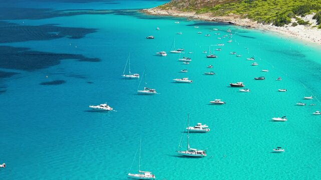 Luxury yachts anchored in Saleccia bay aerial 70mm drone shot in Corsica island France. Tropical Caribbean sea with dramatic mountain background 4K