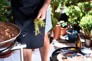 Obraz premium Fresh rosemary ready for seasoning paella during rustic Mediterranean outdoor cooking