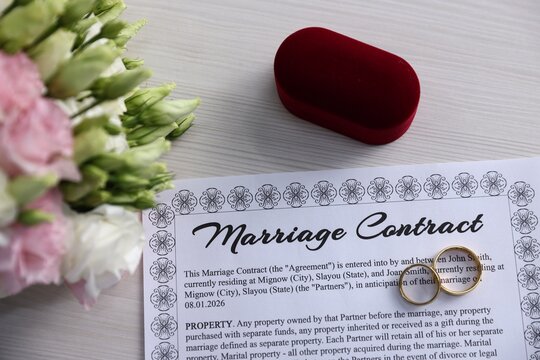 Marriage contract, golden rings and bouquet of flowers on light wooden table, flat lay