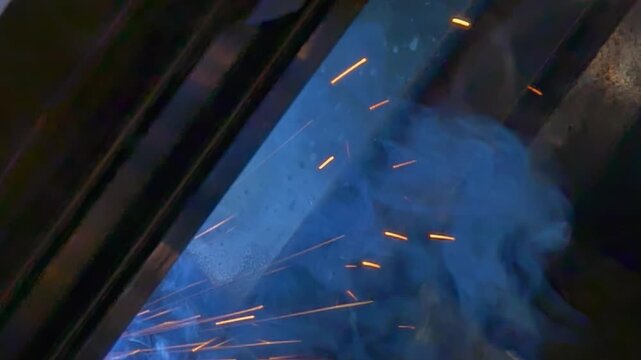 A precision argon welding robot joins metal pipes as the robotic arm follows the working area in an industrial setting. Bright sparks flare around the welding area as the process continues.