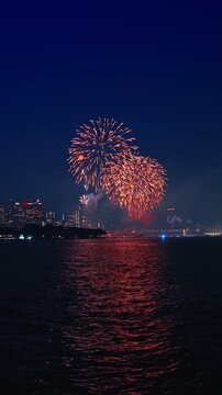 The vibrant explosions illuminate a city skyline at night. Fireworks in New York City, USA. Vertical video.