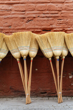 Straw brooms lined against red brick wall