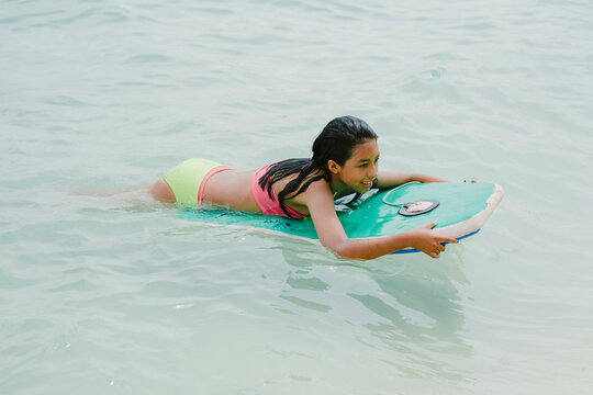 Young girl bodyboarding in ocean on summer vacation