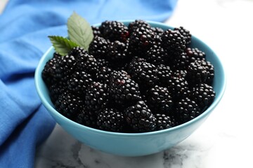 Many fresh blackberries and green leaves in bowl on light marble table, closeup © New Africa