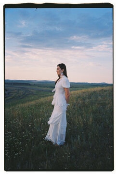 Woman in White Dress Standing in Wild Meadow at Sunset
