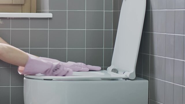 Close-up of hands in rubber gloves cleaning toilet bowl with brush and detergent