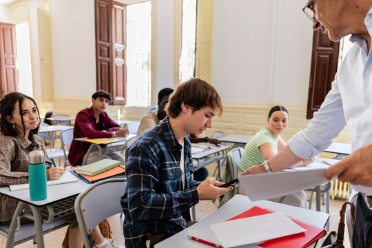 Teacher distributing papers to students in university classroom