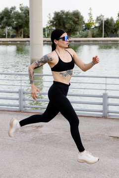 Full-body shot of a female athlete training solo by a park lake