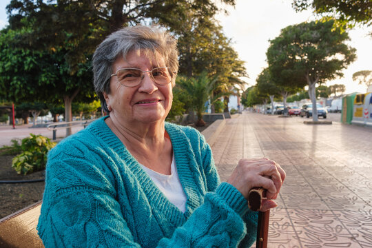 Senior woman smiling on a park bench holding a walking stick
