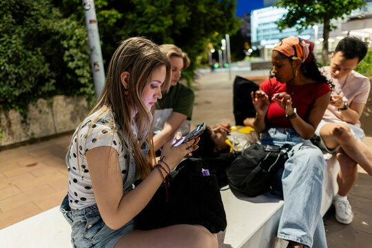 Young diverse friends using smartphones together on urban bench