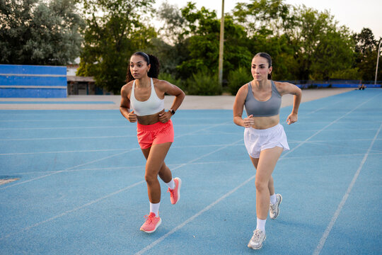 Two determined women running on blue track