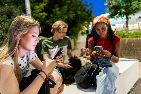 Young people immersed in smartphones ignoring each other outdoors