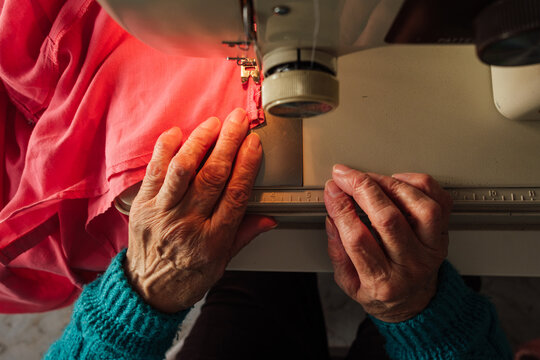 Senior woman's hands sewing red fabric on machine