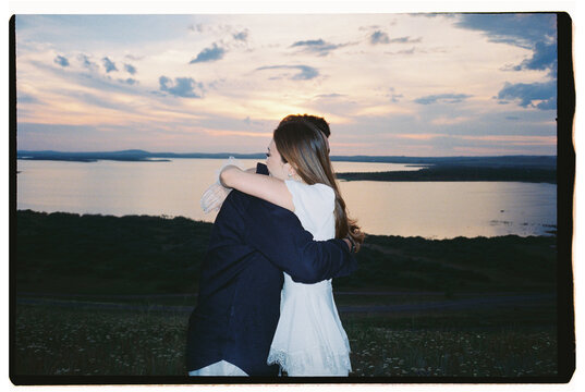 Couple Embracing After Engagement at Sunset by the Lake