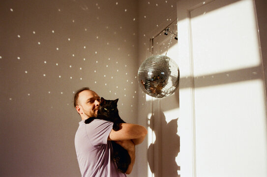Man holds black cat with disco ball in the room