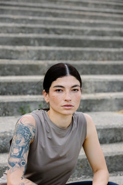 Athletic woman in sportswear sitting on park steps, looking at camera