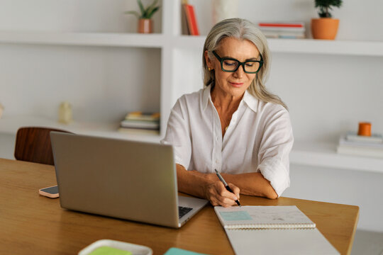 Woman taking notes while working on laptop at home