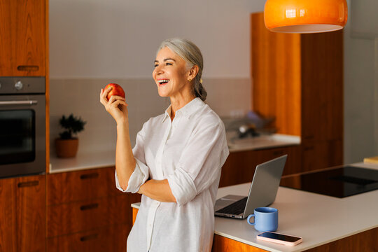 Woman smiling holding red apple in modern kitchen