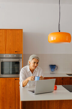 Senior woman working from home in kitchen using laptop
