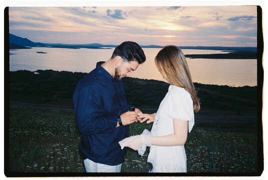 Man Placing Engagement Ring on Woman's Finger at Sunset by the Lake