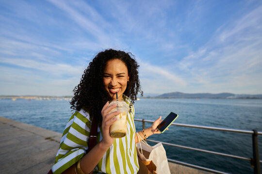 Young woman enjoying iced coffee and shopping by the sea
