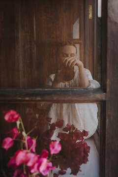 Moody portrait of female photographer taken through window frame.