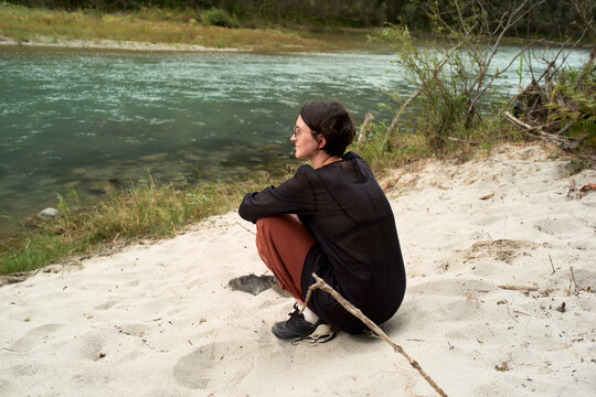 Young Woman Sits by River on Sandy Bank