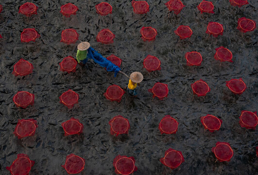 Two unidentified persons working with fishing nets on a muddy river bed.