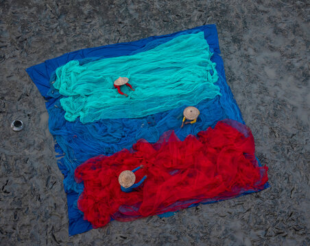 Unidentified fishermen arranging colourful fish nets on muddy riverbed. Top view, selective focus