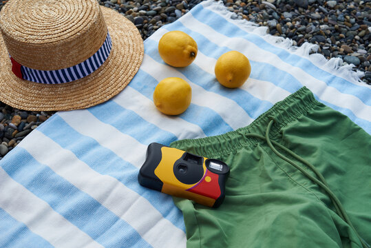 Beach setting with a hat, lemons, and disposable camera on a towel