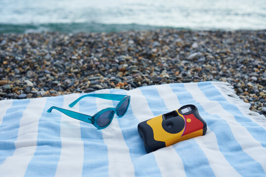 Disposable camera and sunglasses on a striped beach towel
