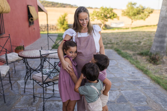 Happy pregnant mother hugging her three children outdoor at home
