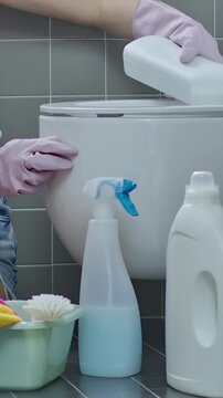 Close-up of hands in rubber gloves cleaning toilet bowl with brush and detergent