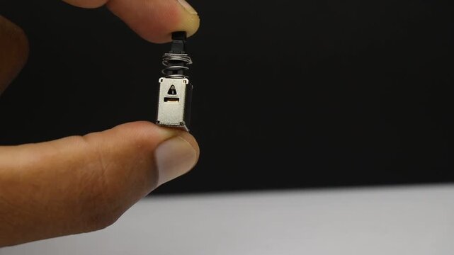 Switch component held in fingers showing the spring loaded button used to turn a circuit on or off with a single press