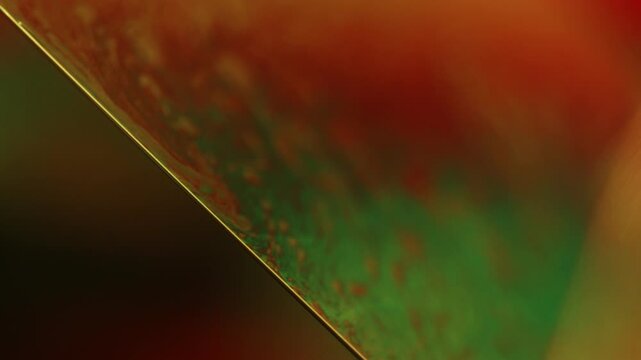 Inclined liquid film facet with razor specular edge and crimson to green marbling. A low-key macro photograph capturing a crisp diagonal specular edge bisecting a liquid film facet