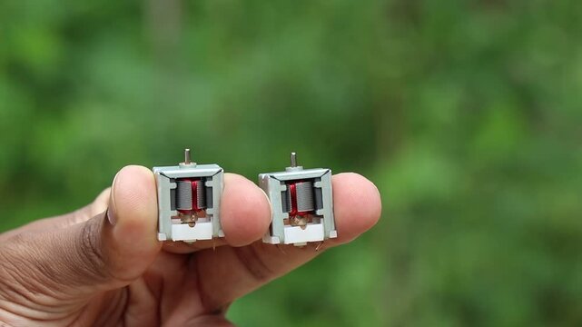 Dc motor with single shaft and visible internal parts held in the hand on natural light background