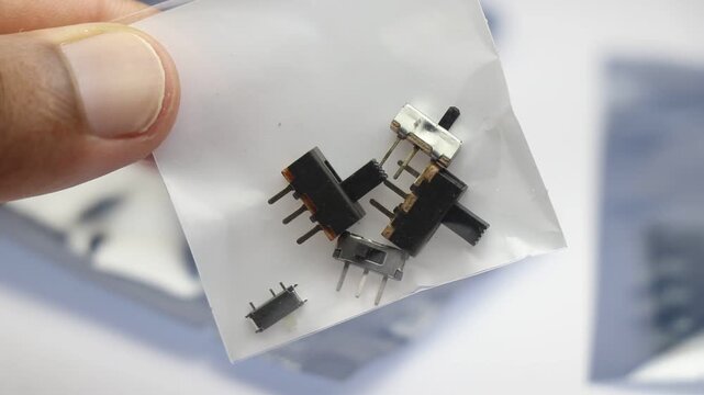 Mini slide switches of different sizes on a clear plastic bag held in the hand