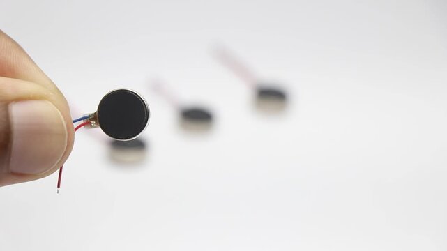 Coin type micro vibration motor held in hand with other motors blurred in background