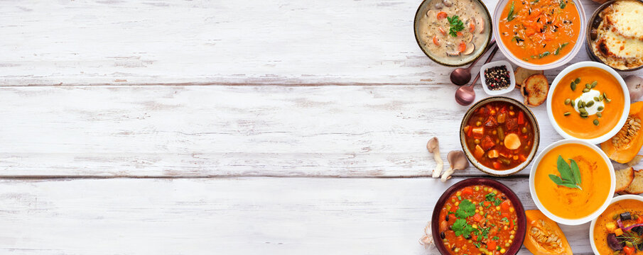 Variety of delicious homemade warm and cozy autumn soups. Top view side border on a white wood banner background. Pumpkin, squash, sweet potato, mushroom, French onion and hearty vegetable.