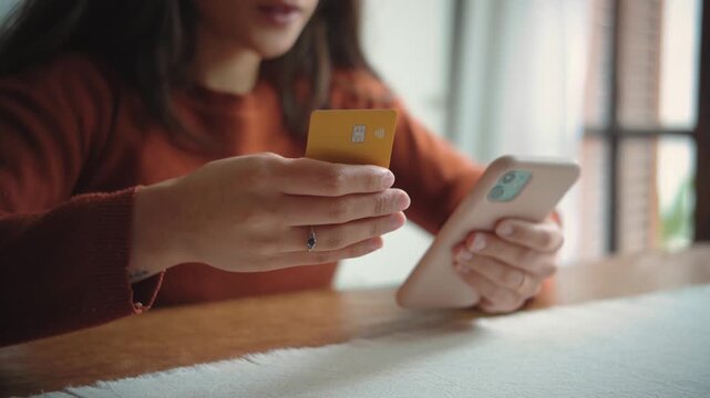 Close-up of an anonymous woman&rsquo;s hand holding a credit card for online shopping at home, highlighting digital commerce, consumer spending, and secure payment.
