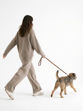 Rear view of a woman in gray casual loungewear walking her fluffy dog on a leash, isolated on white background.-1