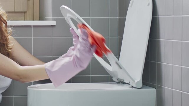 Exhausted young woman stopping toilet cleaning to check smartphone and smiling
