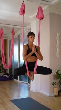 Woman meditating with hands together while balancing in a suspended aerial yoga hammock