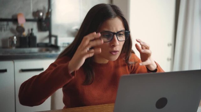 Young Latina woman sitting at home using her laptop while feeling very frustrated and angry, highlighting stress, technology problems, and emotional tension.
