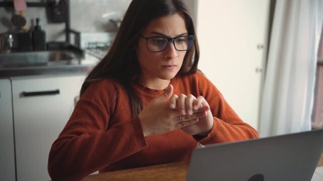 Young Latina woman using her laptop at home while biting her nails from anxiety, highlighting stress, worry, digital pressure, and emotional tension.
