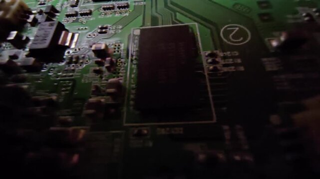 Detailed close-up camera motion over a green projector mainboard PCB showing microchips, capacitors, trace paths, and a ribbon cable connector. Ideal for home theater equipment repair