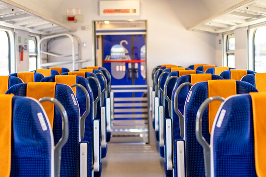 Empty train carriage interior shows rows of blue and orange seats stretching toward the front. Concept of modern public transportation and clean train interior design for travel content.