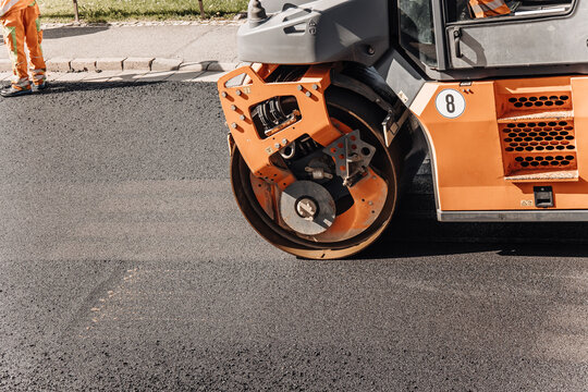 Orange road roller compactor smoothing fresh asphalt pavement close-up
