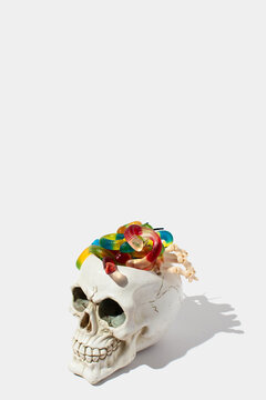 Human skeleton skull with gummy candies in a shape of a snake and fingers on a white background. Halloween scarey and candy concept.